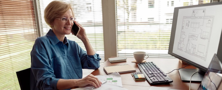 Mature woman engineer constructor talking phone with client while works on project from home office