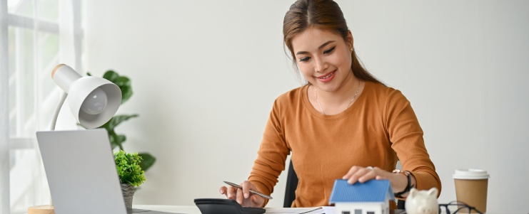 A beautiful and happy Asian female real estate agent working at her desk, calculating the down payment, and working on a letter of guarantee for her clients.